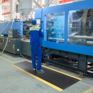 Schwarze KARAT Anti-Ermüdungsmatte Dyna-Protect mit gelbem Rand im Einsatz vor Maschine.