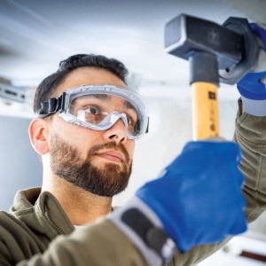 Mann mit LUX-TOOLS Schutzbrille und Band beim Hämmern. Augenschutz für Heimwerker.