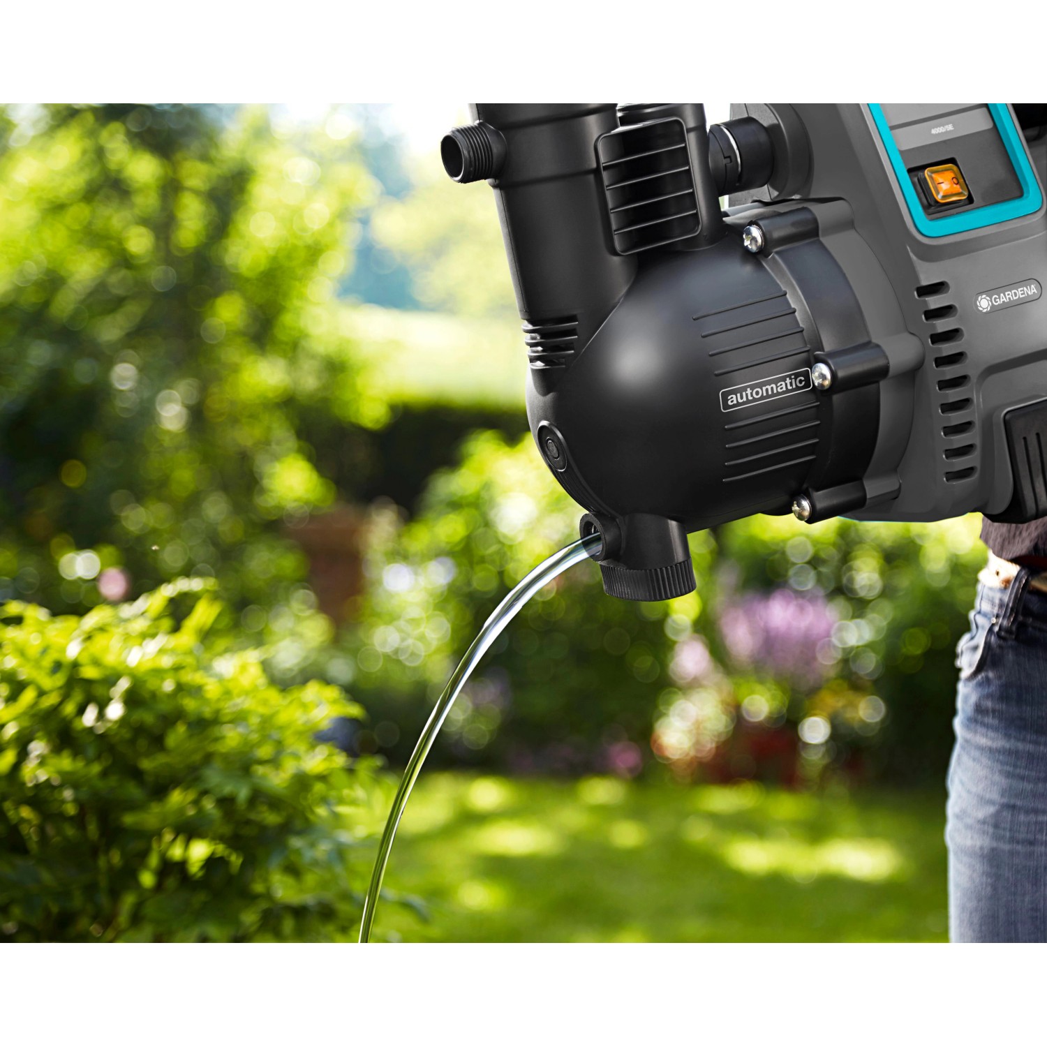 Gardena Haus- und Gartenautomat 4000/5 in Aktion: Wasserstrahl aus der Pumpe vor Gartenkulisse.