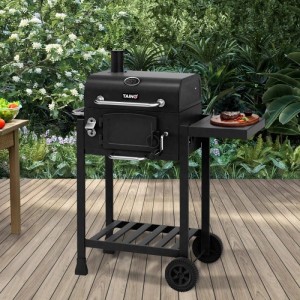 Schwarzer Taino Hero Holzkohlegrill Smoker mit Haube, Seitentisch mit Steak und Rädern auf Holzterrasse im Garten.