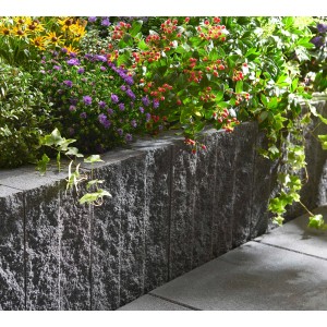 Graphitfarbene Montania Mauer aus Beton mit Bruchsteinoptik als Beetbegrenzung mit Bepflanzung.