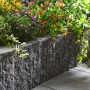 Graphitfarbene Montania Mauer aus Beton mit Bruchsteinoptik als Beetbegrenzung mit Bepflanzung.