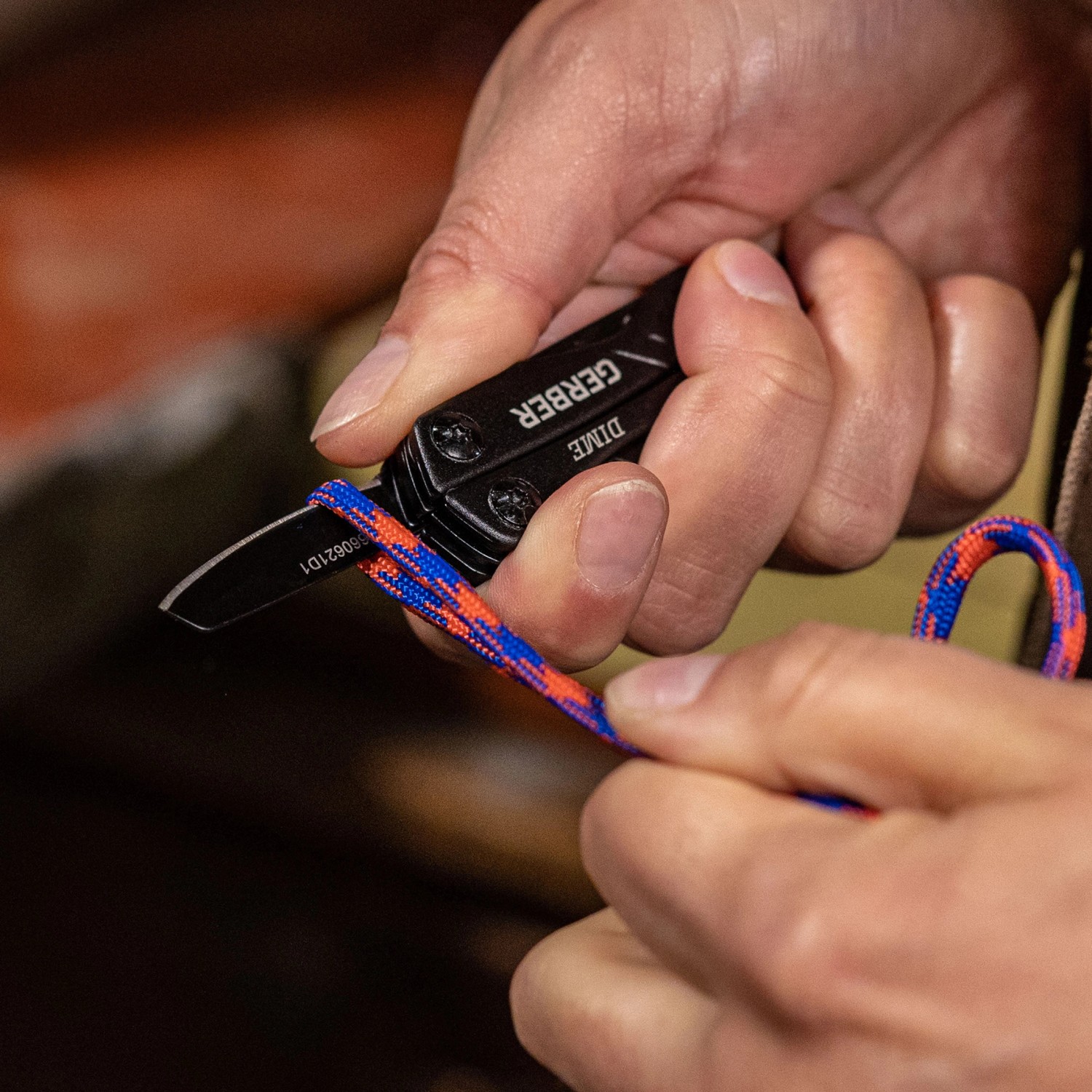 Gerber Multi-Tool Dime: Hände schneiden Seil mit der Klinge des schwarzen Multitools.