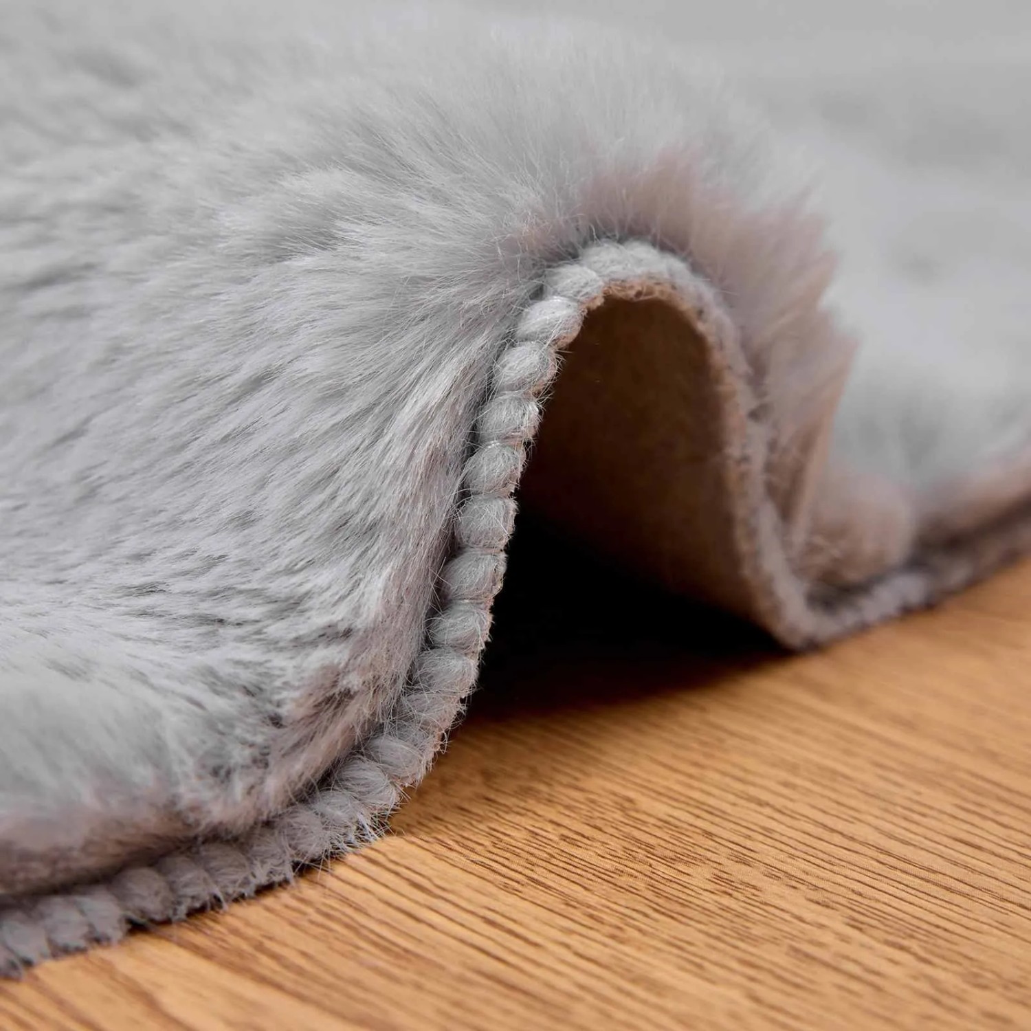 Grauer, runder Kunstfell Teppich Olite aus Polyester. Weiche, flauschige Textur auf Holz. Gemütlicher Bodenbelag.