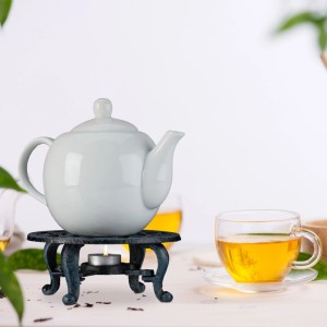 Graues Gusseisen Stövchen mit Teelicht, Teekanne und Teetasse. Dekorativer Teewärmer im Vintage-Design.