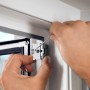 Montage des weißen Tesa Fliegengitter Adapter-Sets am Alu-Türrahmen mit Schraubendreher.