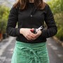 Frau hält Felco Ernte- und Leseschere 322 (19 cm) in den Händen, im Hintergrund Pflanzen.