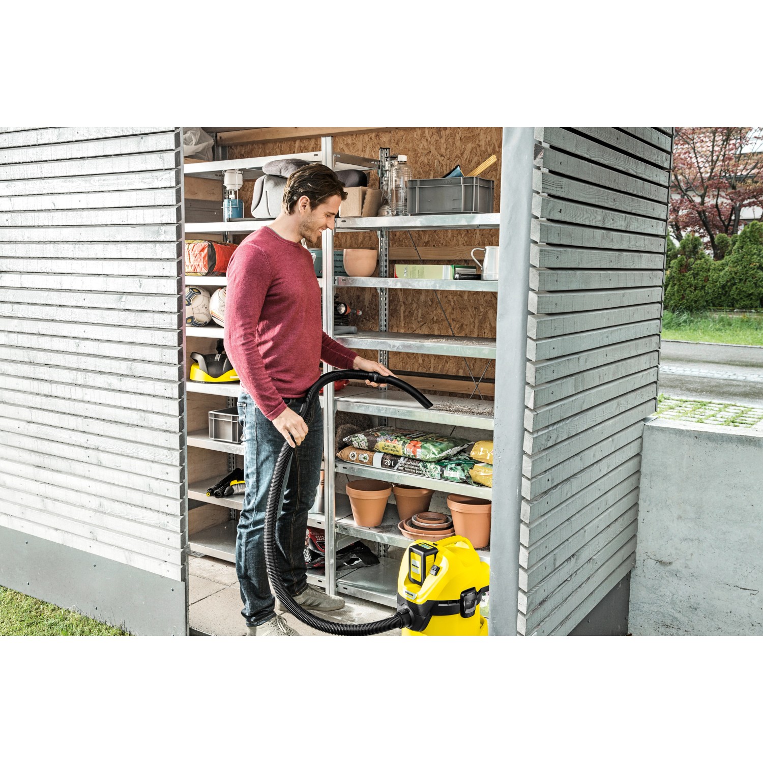Mann saugt mit gelbem Kärcher Akku-Mehrzwecksauger WD 3 Battery Set ein Regal im Gartenhaus.