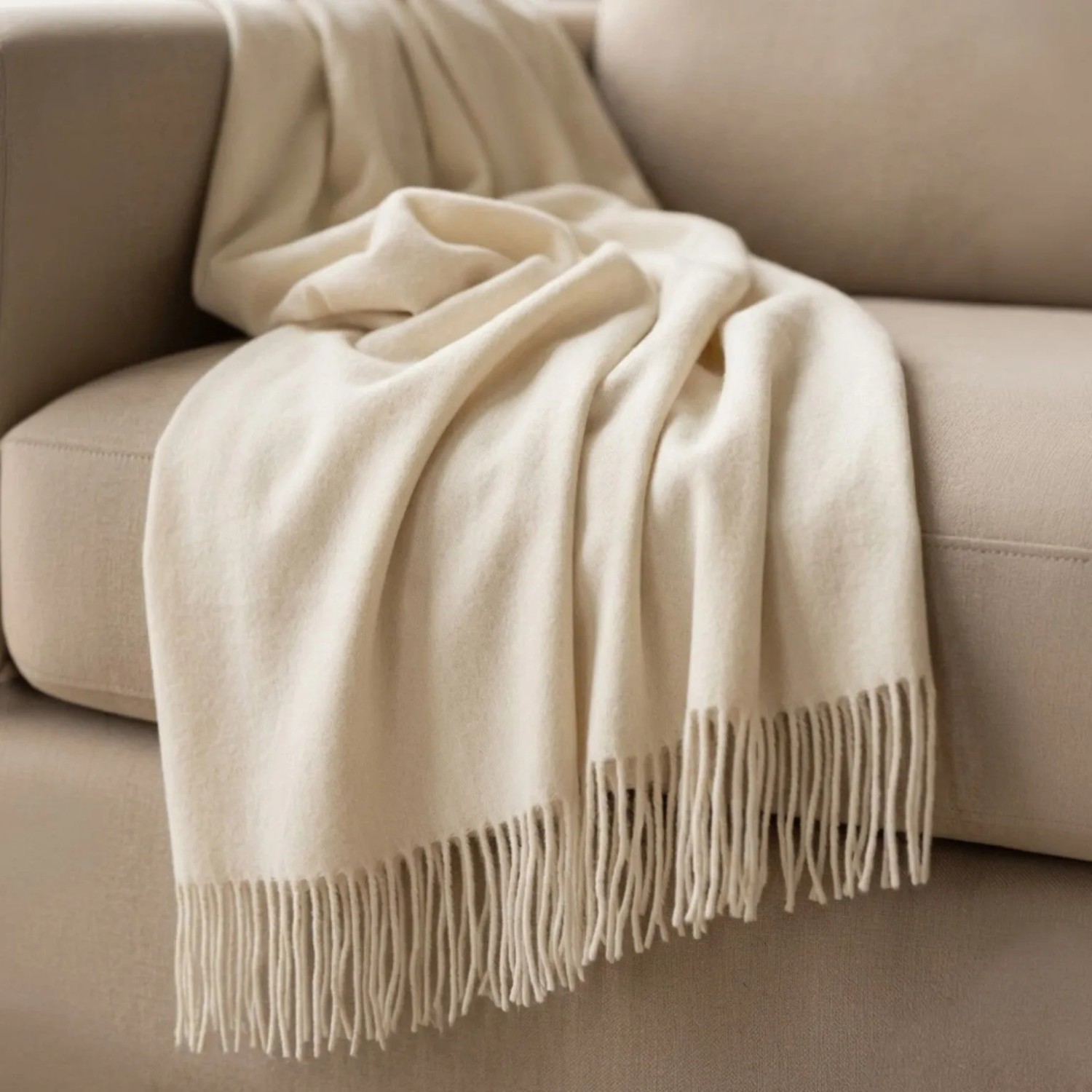 Elfenbeinfarbene Sofadecke aus Baumwoll-Mix mit Fransen, elegant über einem Sofa. Vielseitige Wohndecke.