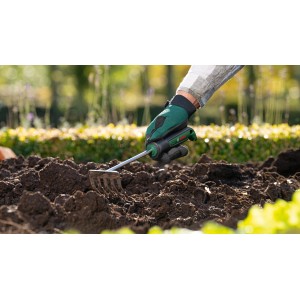 Bosch Garten-Kleinrechen im Einsatz: Hand mit Gartenhandschuh lockert Erde im Gartenbeet.