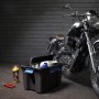 Schwarze Aufbewahrungsbox Scuba M mit Werkzeug und Motorrad im Hintergrund.
