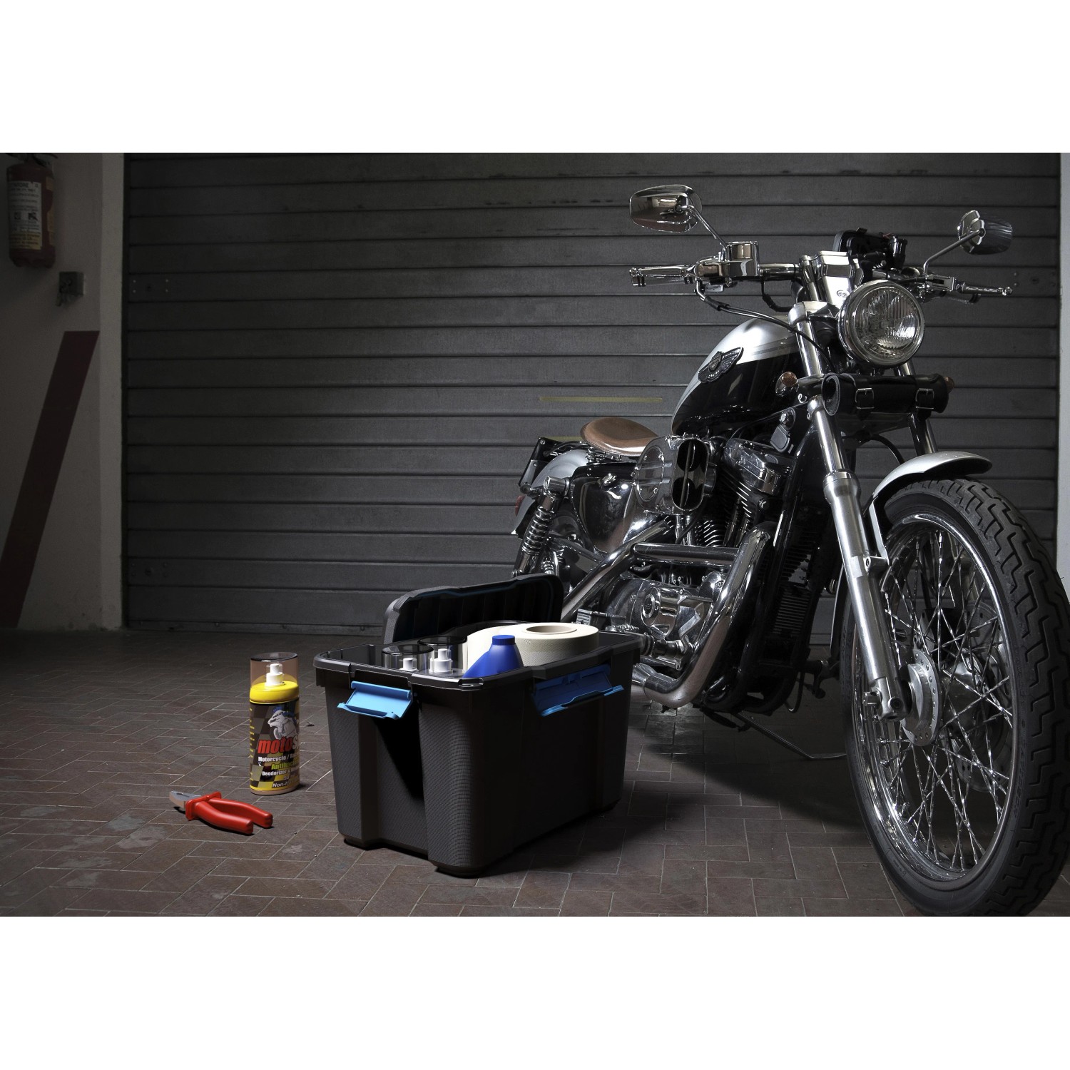 Schwarze Aufbewahrungsbox Scuba M mit Werkzeug und Motorrad im Hintergrund.