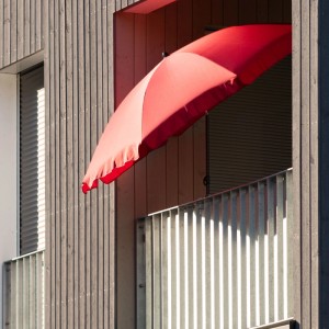 Roter Sonnenschirm mit osoltus Halter am Balkongeländer. Schwarzes Klemmsystem für platzsparende, stabile Befestigung.