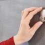 Hand befestigt Tesa Powerstrips Haken Waterproof Zoom Edelstahl an grauer Fliese.