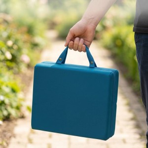 Person trägt faltbare dunkelgrüne Garten Kniematte mit Tragegriffen auf einem Weg. Knieschutz für Garten & Werkstatt.
