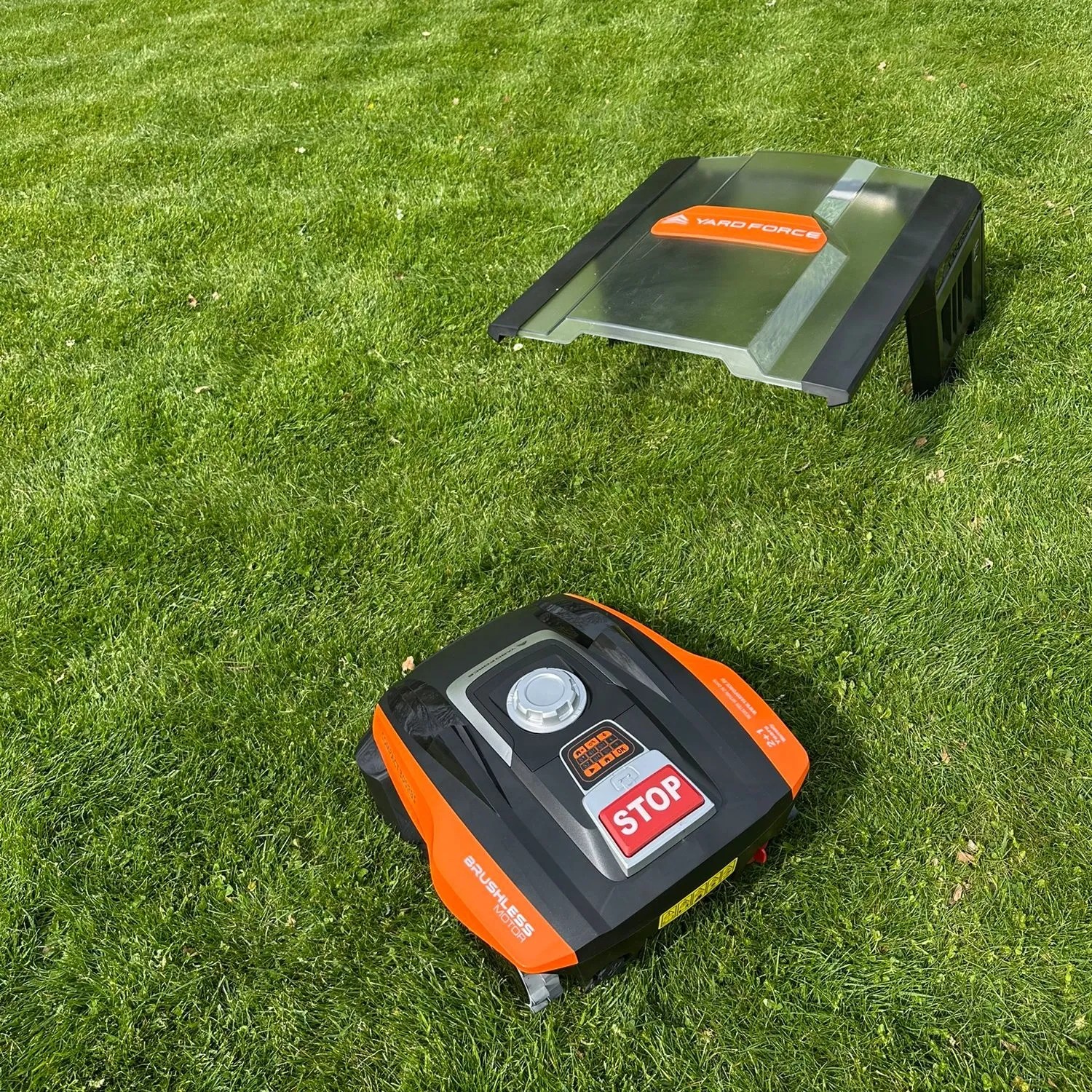 YARD FORCE Mähroboter Compact 300RBS und Garage auf Rasen. Orange-schwarzer Rasenmähroboter, transparente Schutzgarage.