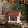 CULT at home Vogel Futterhaus aus hellem Holz mit rustikalem braunem Holzdach, gefüllt mit Futter, hängt im Garten.