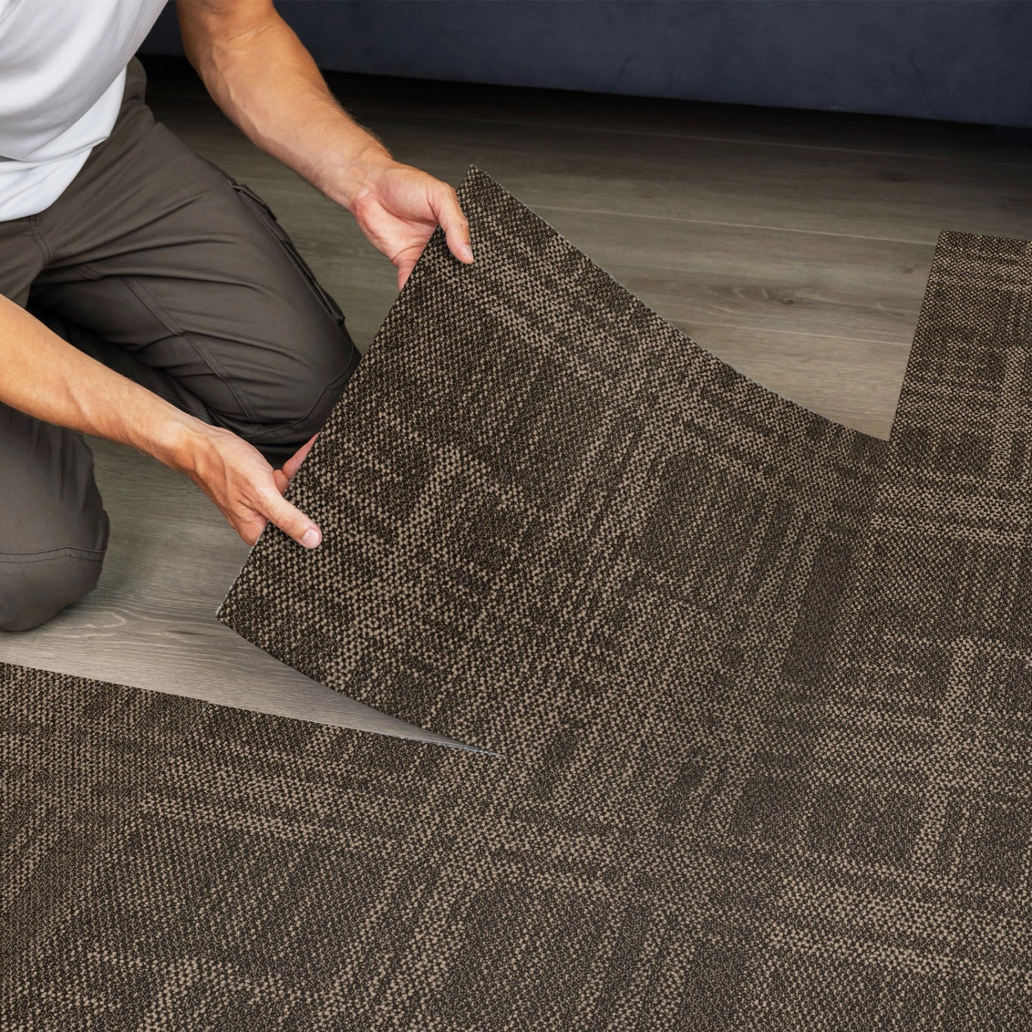 Verlegen von beigen Floordirekt Teppichfliesen Luzern 50x50 mit Streifenmuster.