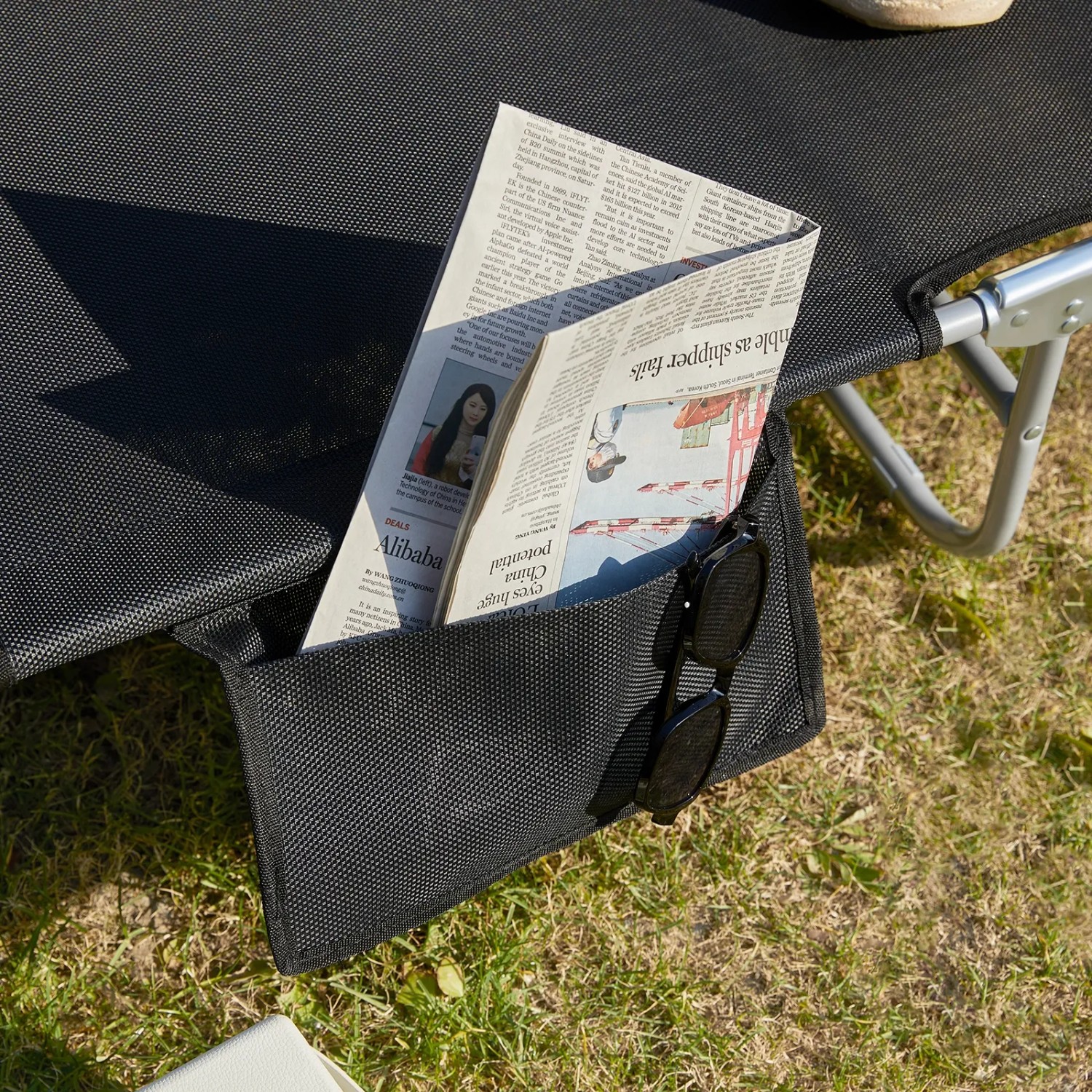 Detailaufnahme: Schwarze SoBuy Gartenliege mit Seitentasche für Zeitung und Sonnenbrille.