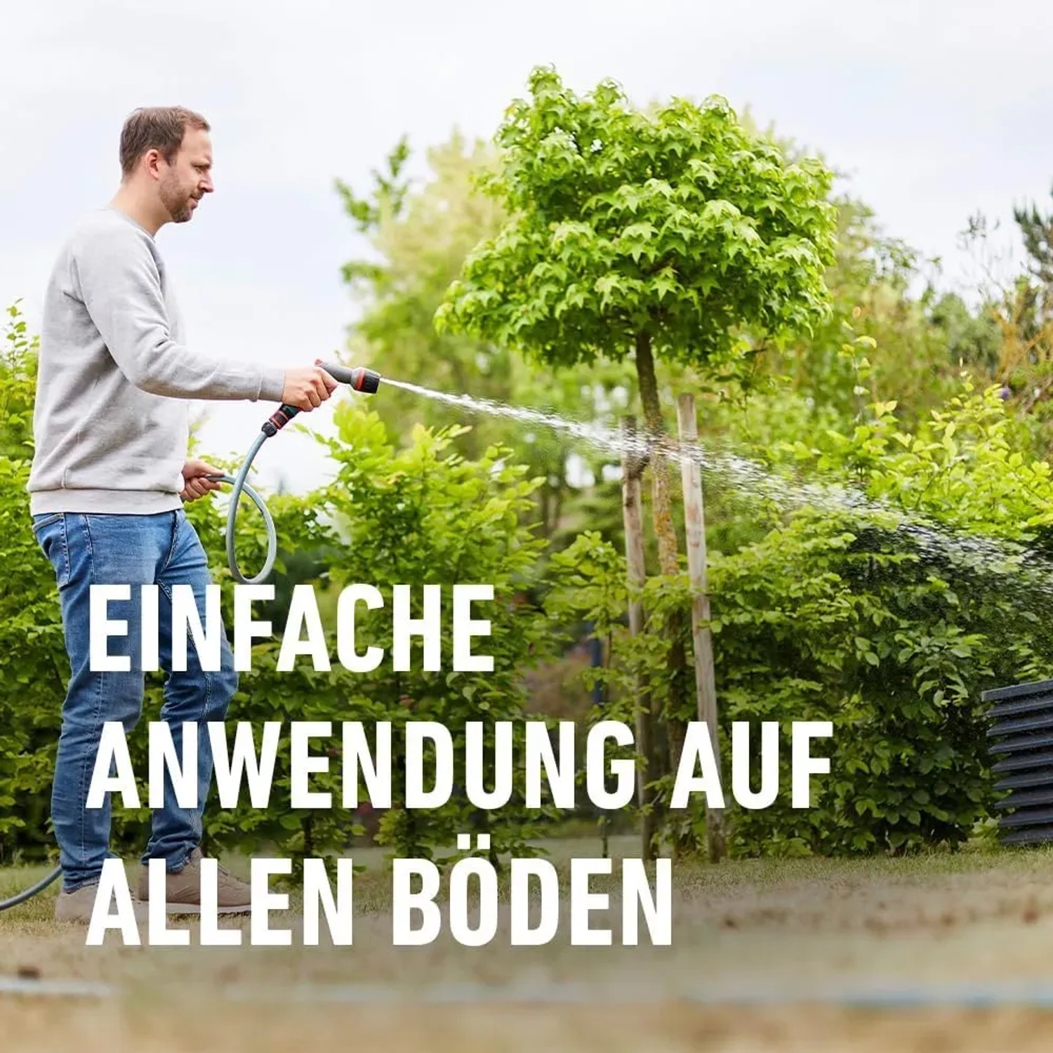 Anwendung von Compo Rasen Nachsaat Turbo: Mann bewässert Rasenfläche mit Gartenschlauch.