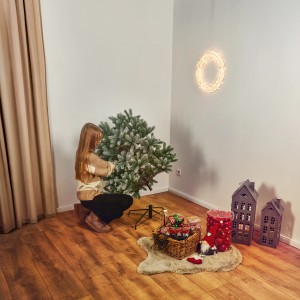 Mädchen baut Kunsttanne Blavand 120 cm auf, geschmückt mit Kunstschnee und Zapfen, für Weihnachten.