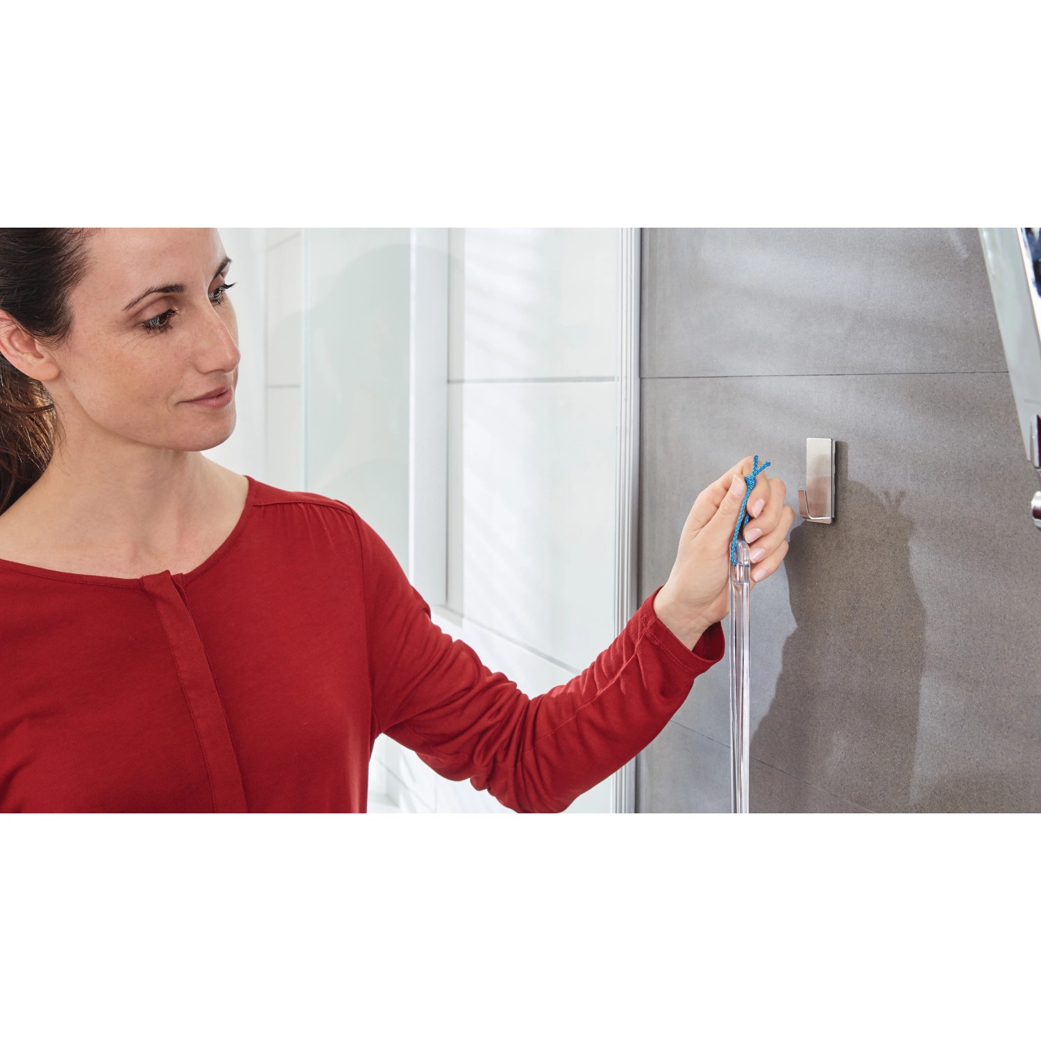 Frau hängt Duschabzieher an Tesa Powerstrips Haken Waterproof Edelstahl im Bad auf.