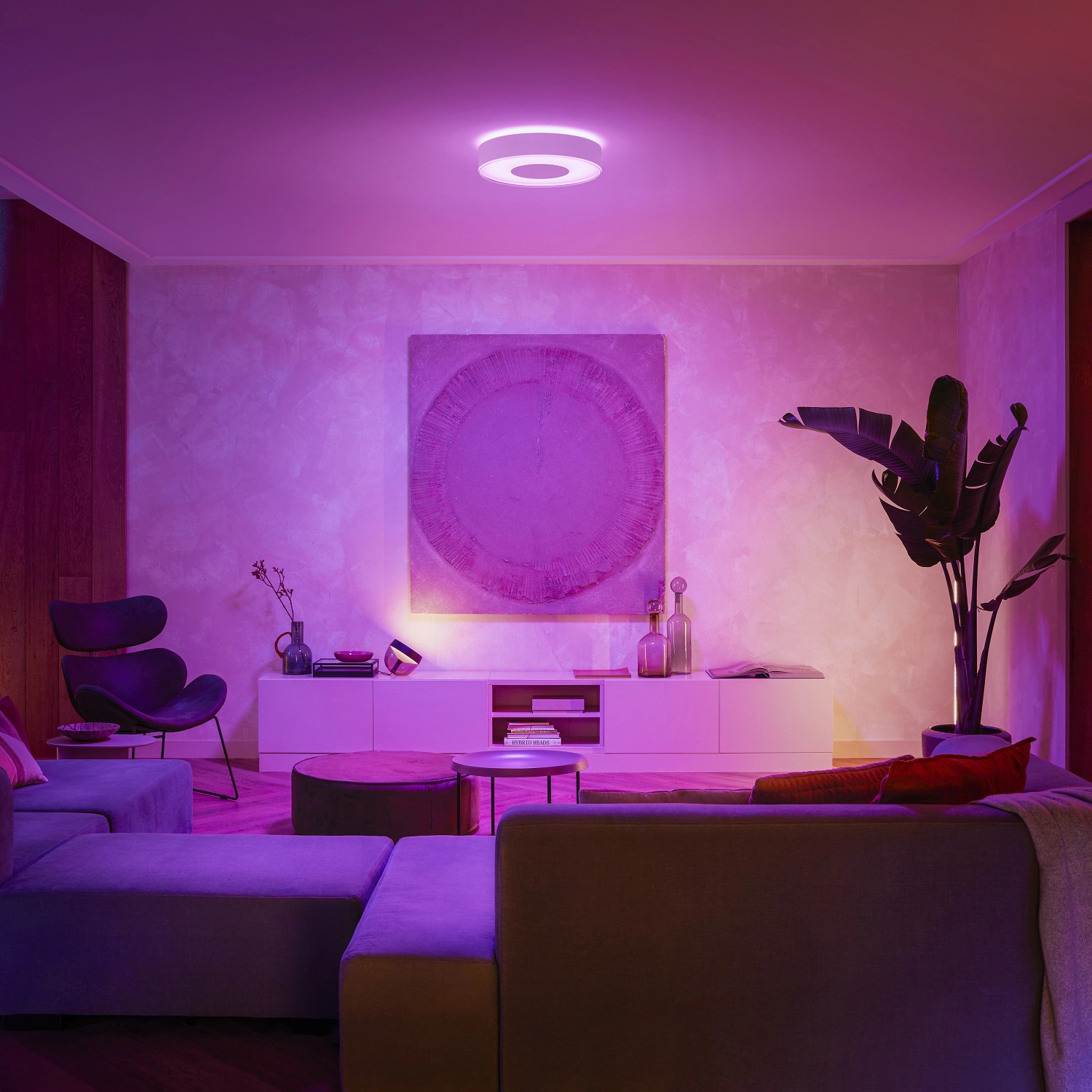 Weiße Philips Hue Infuse Deckenleuchte M im Wohnzimmer mit farbiger Ambiente-Beleuchtung.