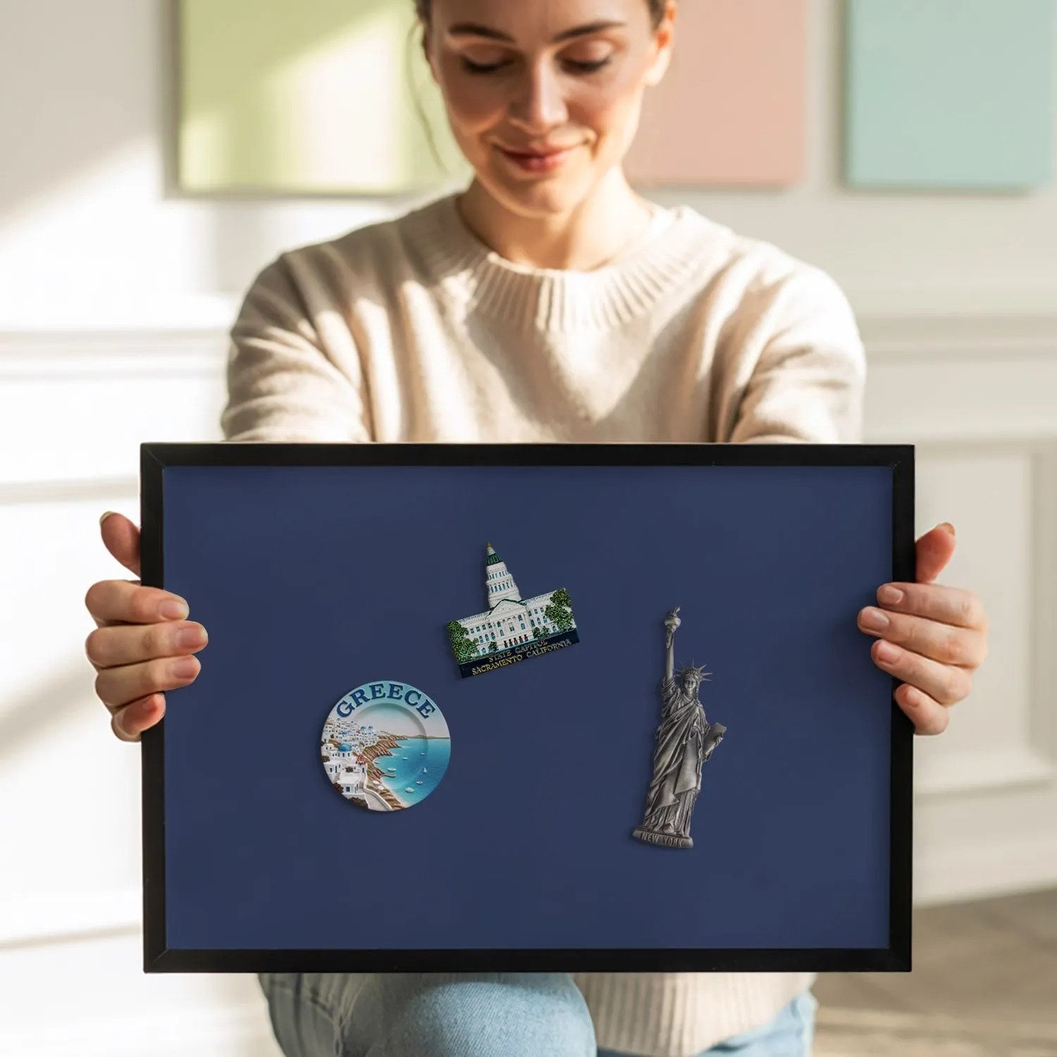 Frau präsentiert marineblaue Magnettafel mit schwarzem Rahmen, bestückt mit Reisemagneten. Praktische Magnetpinnwand für Notizen.