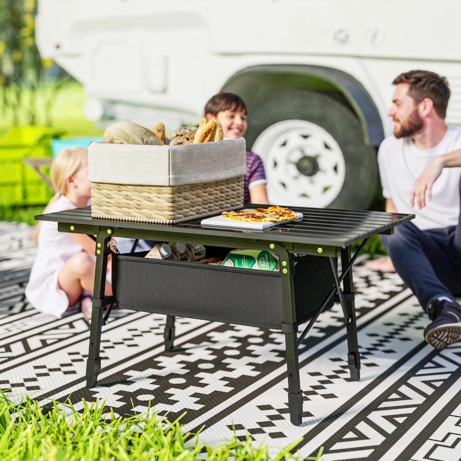Schwarzer Outsunny Campingtisch aus Aluminium mit Korb und Familie beim Picknick.