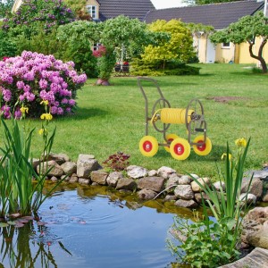 Brauner Relaxdays Schlauchwagen aus Stahl mit gelbem Schlauch auf Rasen im Garten. 4 Räder für mobile Bewässerung.