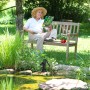 Dekorative, schwarze Gartenpumpe aus Gusseisen am Teich, Frau liest auf Bank im Hintergrund.