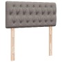 Gepolstertes, graues Boxspringbett-Kopfteil mit Knöpfen und Holzfüßen.