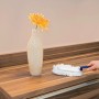 Staubfanggerät Mikrofaser in Nutzung auf Holzoberfläche, neben Vase mit Blume.