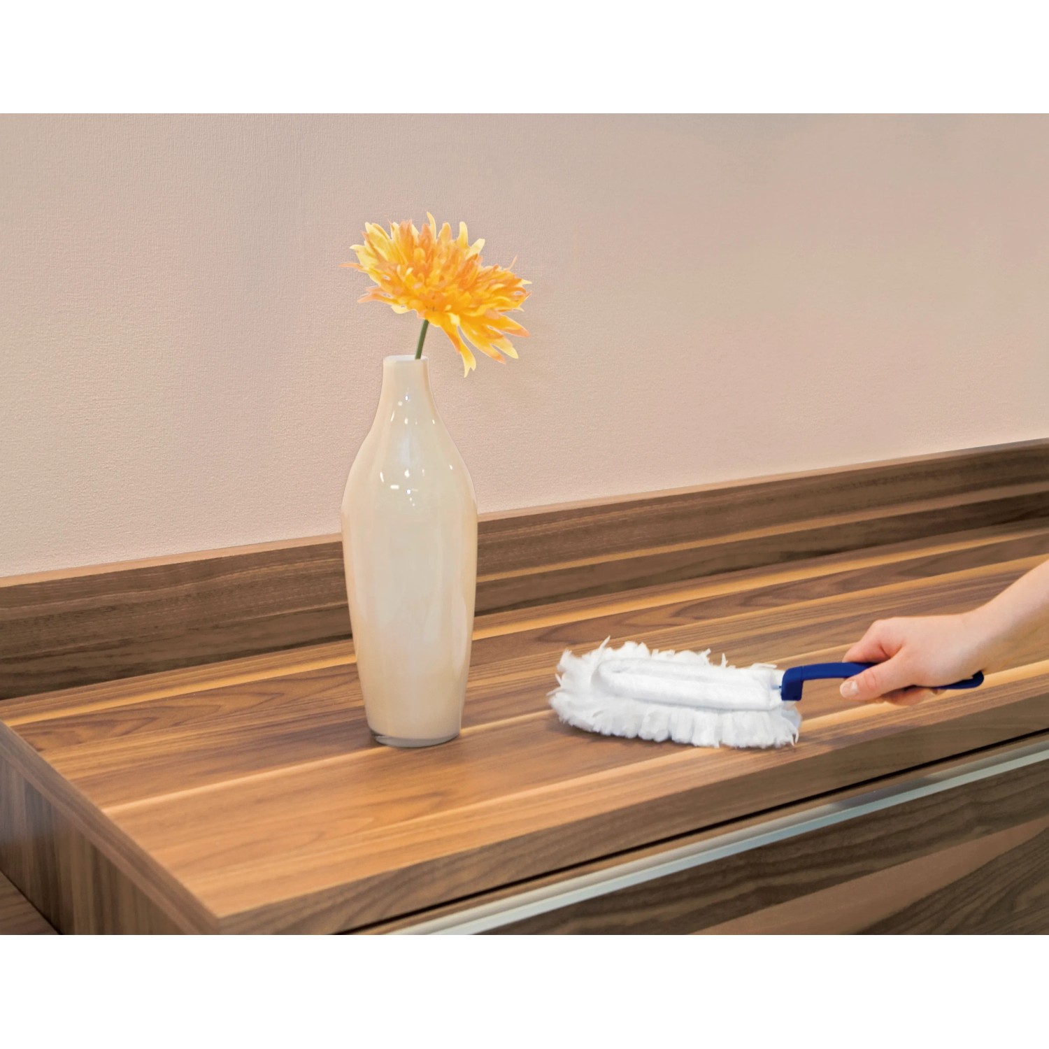 Staubfanggerät Mikrofaser in Nutzung auf Holzoberfläche, neben Vase mit Blume.