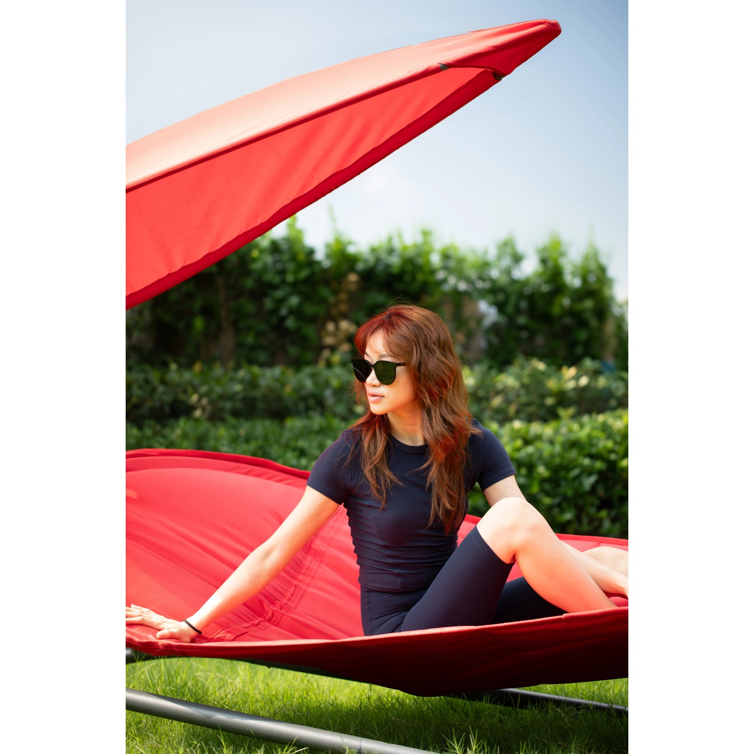 Frau entspannt in roter Leco Luxus-Hängematte Gloria mit Sonnendach im Garten.