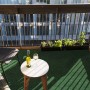 Grüner Primaflor Rasenteppich auf einem Balkon mit Tisch und Stuhl.