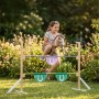 Mädchen springt mit Steckenpferd über höhenverstellbares Hobby Horse Hindernis aus Holz in Natur, Violett, Türkis im Garten.