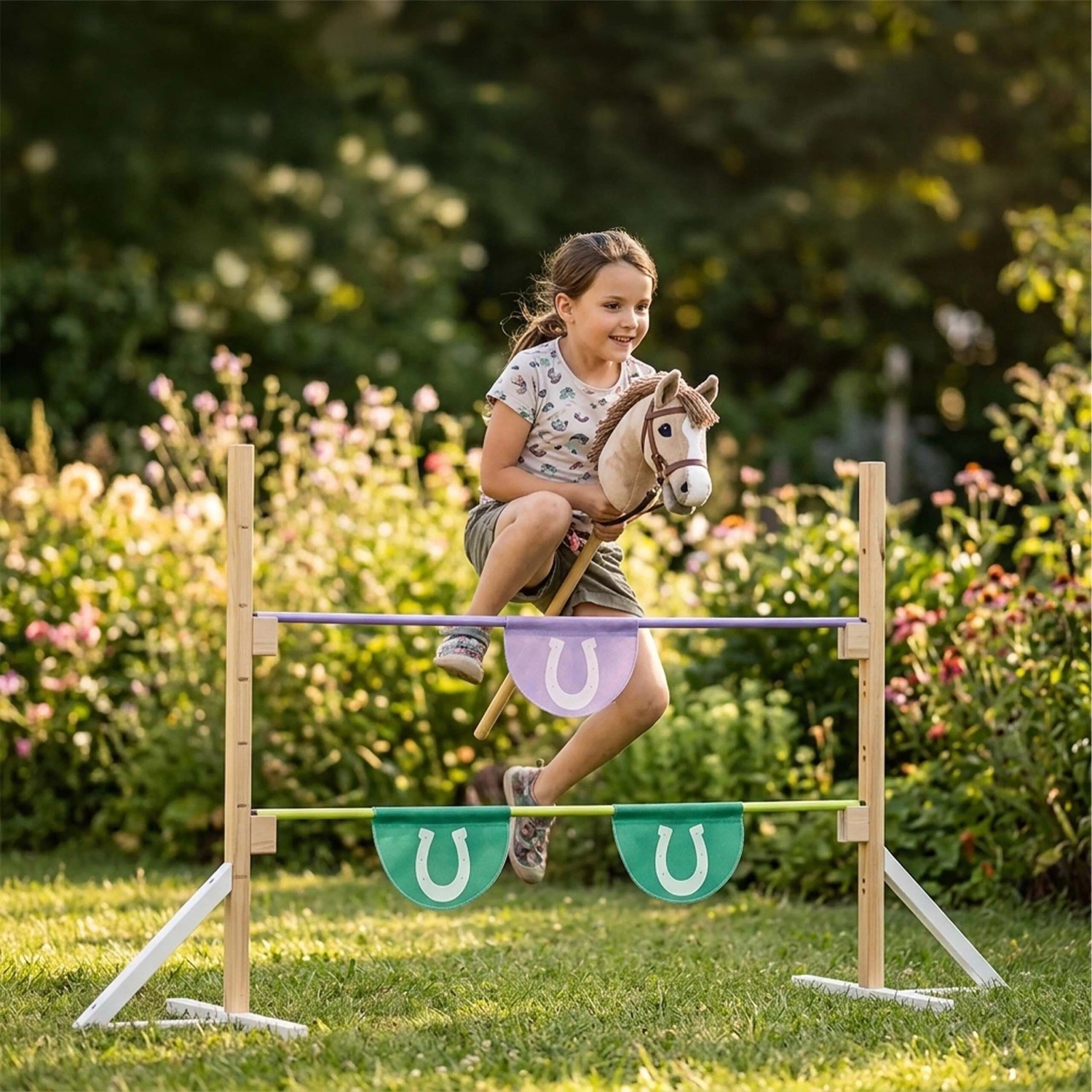 Mädchen springt mit Steckenpferd über höhenverstellbares Hobby Horse Hindernis aus Holz in Natur, Violett, Türkis im Garten.