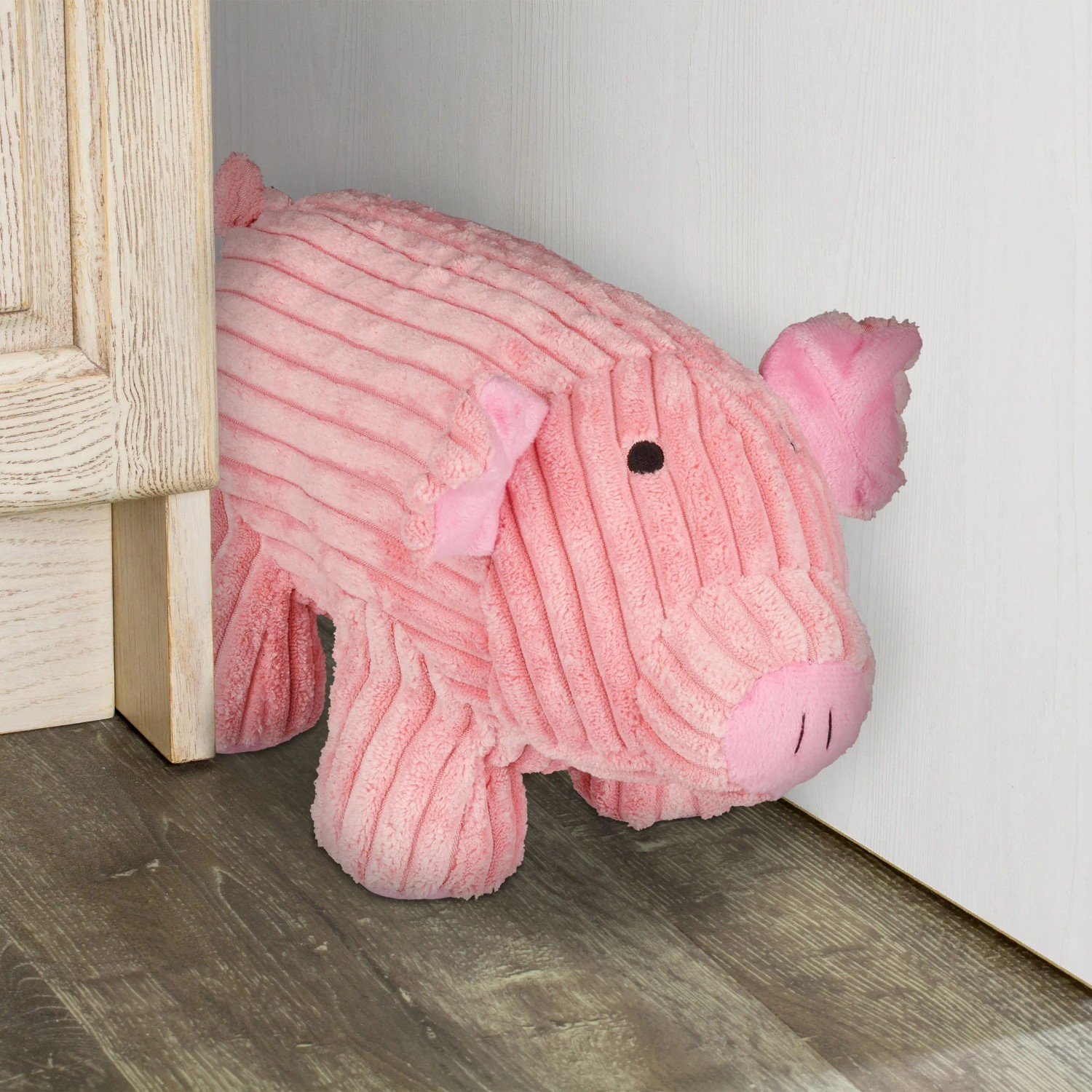 Rosa Plüsch-Türstopper in Schweineform hält eine Tür offen. Dekorativer Türpuffer aus weichem Stoff auf Holzboden.