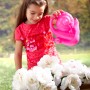 Mädchen gießt Blumen im Blumenkasten mit einer rosa Schnecken-Gießkanne. Zubehör für Gartenspielgeräte.