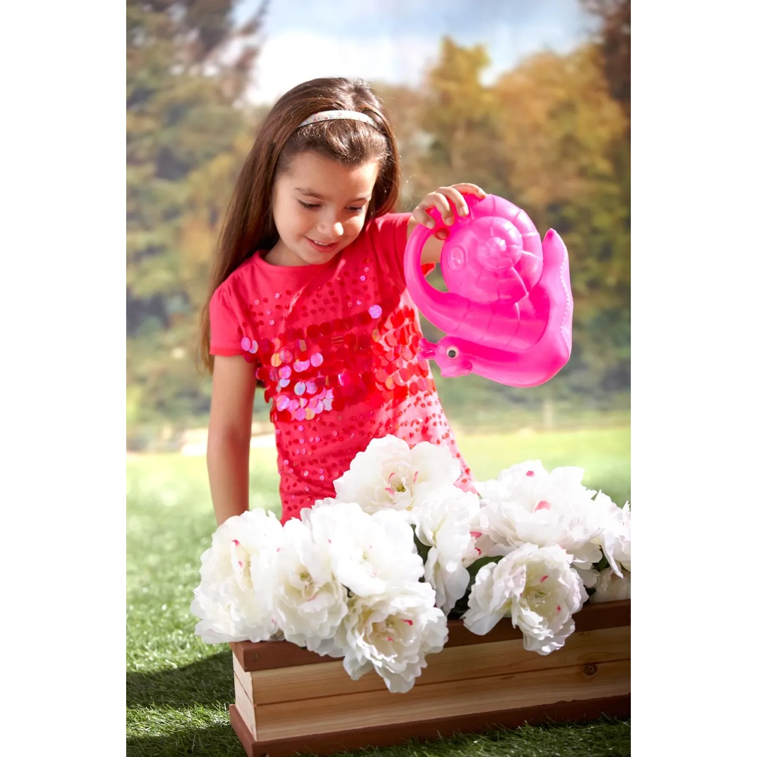 Mädchen gießt Blumen im Blumenkasten mit einer rosa Schnecken-Gießkanne. Zubehör für Gartenspielgeräte.