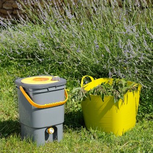 Hozelock Düngermischer Pure Biomix neben gelbem Eimer mit Grünpflanzen im Garten.