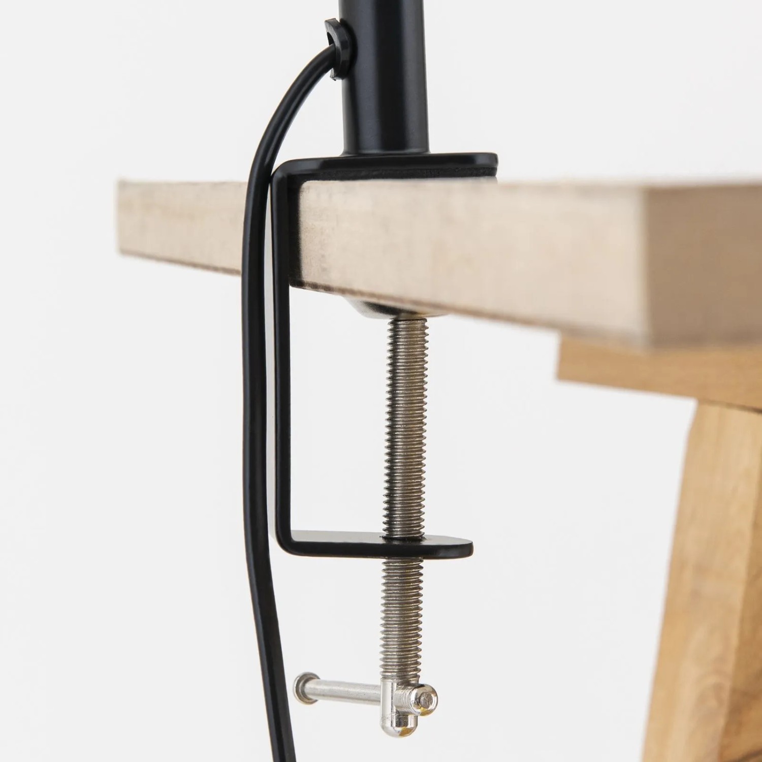 Schwarze Metall-Klemmleuchte Dotty an heller Holzplatte befestigt. Zeigt die Klemmfunktion mit Schraube und Kabel.