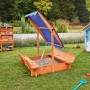 Home Deluxe Sandkasten Buddelkiste mit blauem Dach und Sitzbänken im Garten.