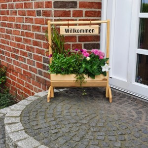 Kleiner Blumenkasten „Willkommen“ aus Kiefernholz, bepflanzt mit bunten Blumen, vor einer Haustür.