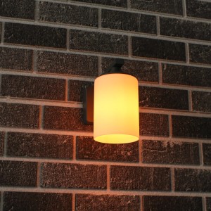 Anthrazitfarbene LED Außenwandleuchte mit zylindrischem Lampenschirm an einer Backsteinwand.