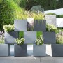 Gestapelte, graue Scheurich C-Cube Pflanzgefäße (38x38 cm) mit Bepflanzung im Garten.