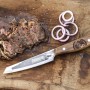 Petromax Allzweckmesser mit 14cm Klinge auf Holzbrett mit Steak und Zwiebelringen.