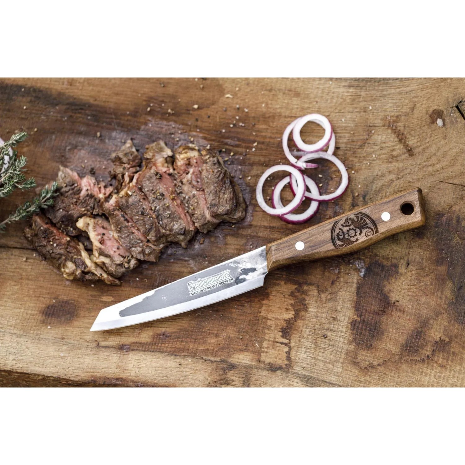 Petromax Allzweckmesser mit 14cm Klinge auf Holzbrett mit Steak und Zwiebelringen.
