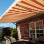 Halbkassettenmarkise Sky Fix, 300x250 cm, orange-rot gestreift, über einer Terrasse mit Sitzgruppe.